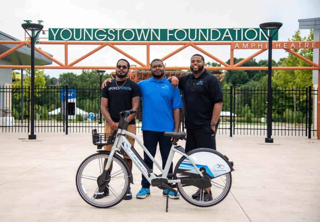 3 male owners of a bikeshare stand with a bike in front of them