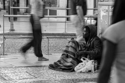 Photograph of a homeless man on the city sidewalk as people rush past black and white photo