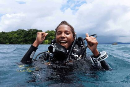 Conservationist naomi longa a man in scuba gear coming up in the water smiling and cheering