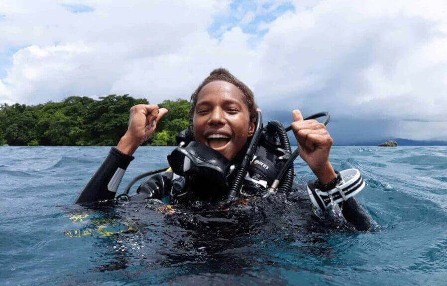 Conservationist naomi longa a man in scuba gear coming up in the water smiling and cheering