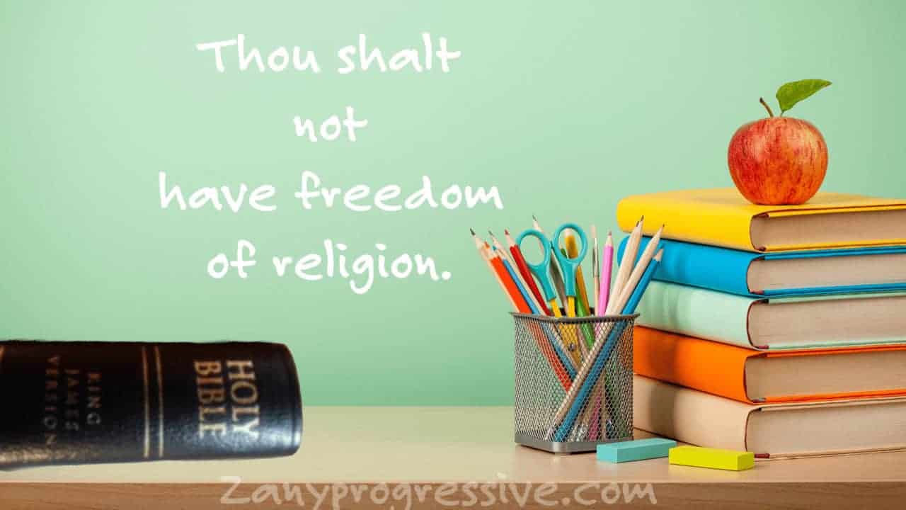 Teachers desk at school with a Bible on it and on the chalkboard behind it i
