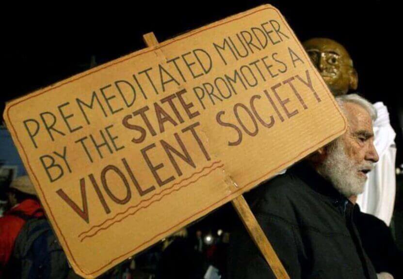 A pro-life protestor with a sign that says “PREMEDITATED MURDER BY THE STATE PROMOTES A VIOLENT SOCIETY”
