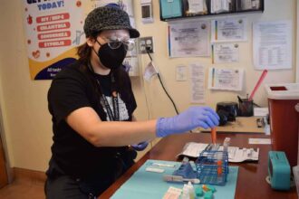 A woman wearing latex gloves and a mask works in a lab