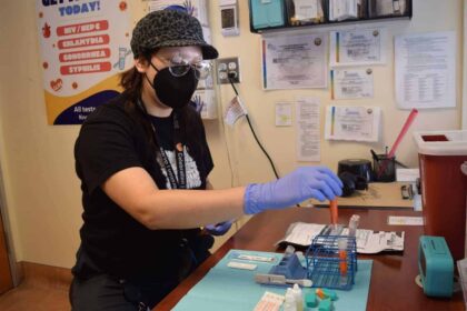 A woman wearing latex gloves and a mask works in a lab