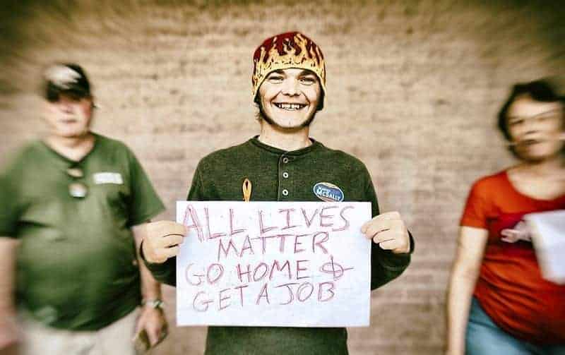 Black lives matter anti-protesta young teen in a knit cap with flames on it holds an all lives matter sign with his parents or grandparents in the background