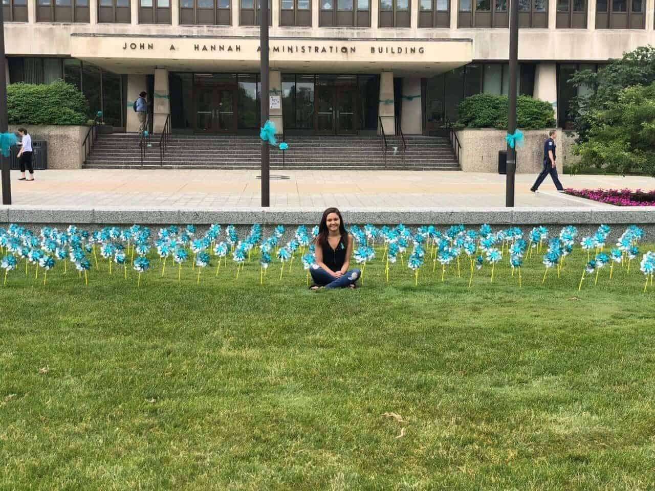 Former gymnast kaylee lorincz sits outside the hannah administration building on michigan state university campus in 2018 surrounded by teal pinwheels placed to represent support for survivors of ex-msu and olympic doctor larry nassar.