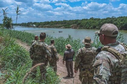Members of the texas national guard watch a border patrol helicopter hover above a group of civilians wading in the rio grande along the texas-mexico border during operation lone star.