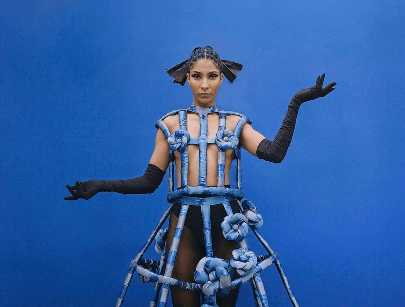 Model on a blue background wearing a futuristic looking light blue dress