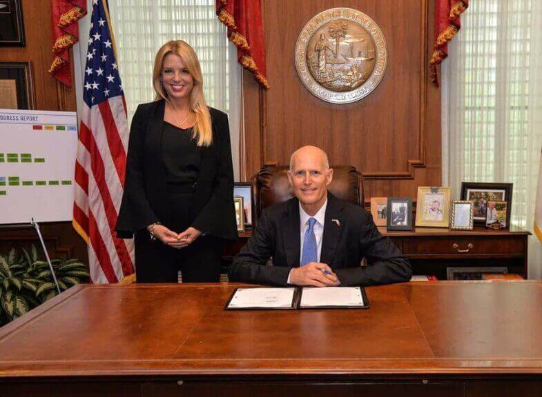 Pam Bondi stands beside Governor Rick Scott during a bill signing.