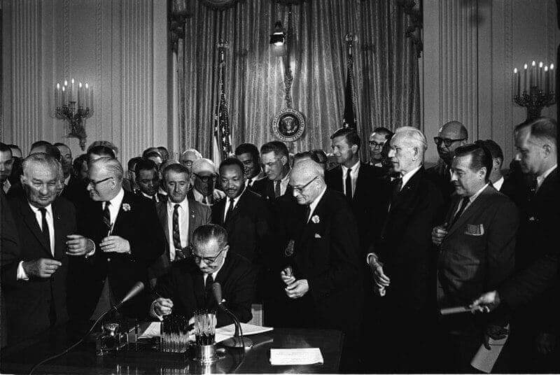 Systemic racism president lyndon b. Johnson signs the 1964 civil rights act as martin luther king, jr. , and others, look on.
