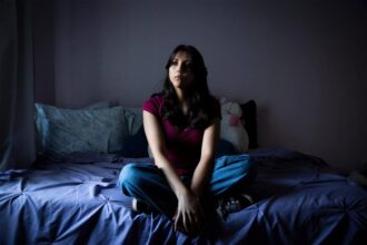 High school student sitting on a bed in her room