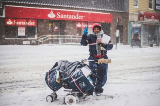 Usps worker standing in the snow-covered street, waves and smiles