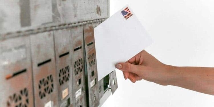A hand puts a letter in a mailbox at the USPS office
