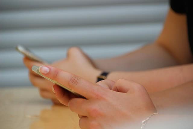 how children and teens should use social media teen hands holding cell phones at a school desk