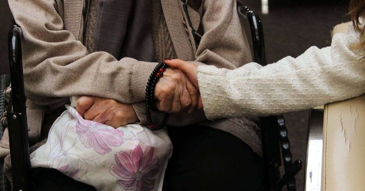 pexels photo 15234225 15234225 00 taken out of his bank account. Elderly woman in wheelchair warmly holding another's hand, symbolizing care and support.