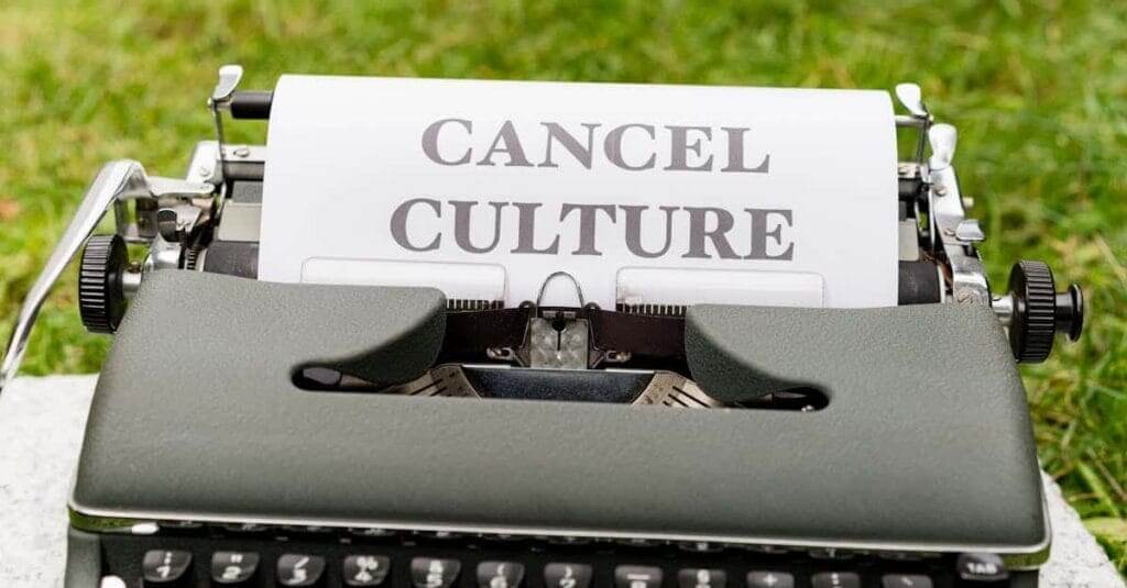 Retro typewriter with 'cancel culture' typed paper on grass background outdoors.