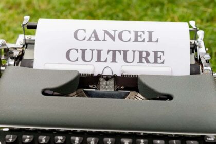 Retro typewriter with 'cancel culture' typed paper on grass background outdoors.