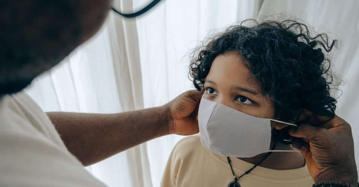 From above unrecognizable black man wearing protective mask on face of ethnic kid standing in room near window closed with curtain