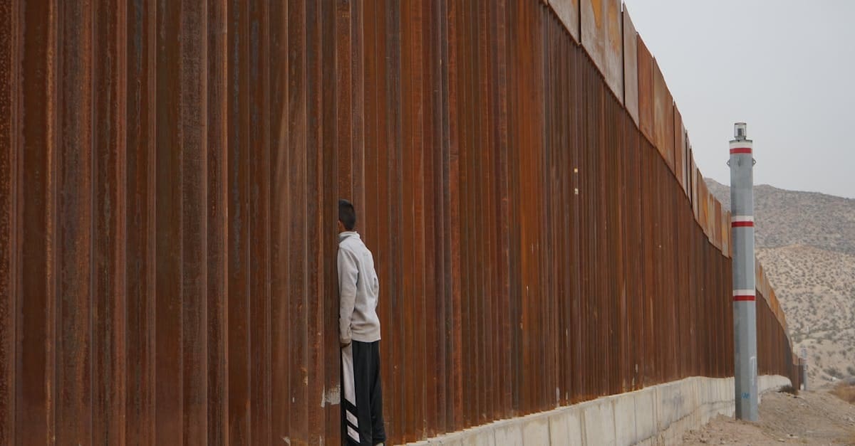 Crossing the us border. A man stands in solitude at a towering border fence in a desert landscape.