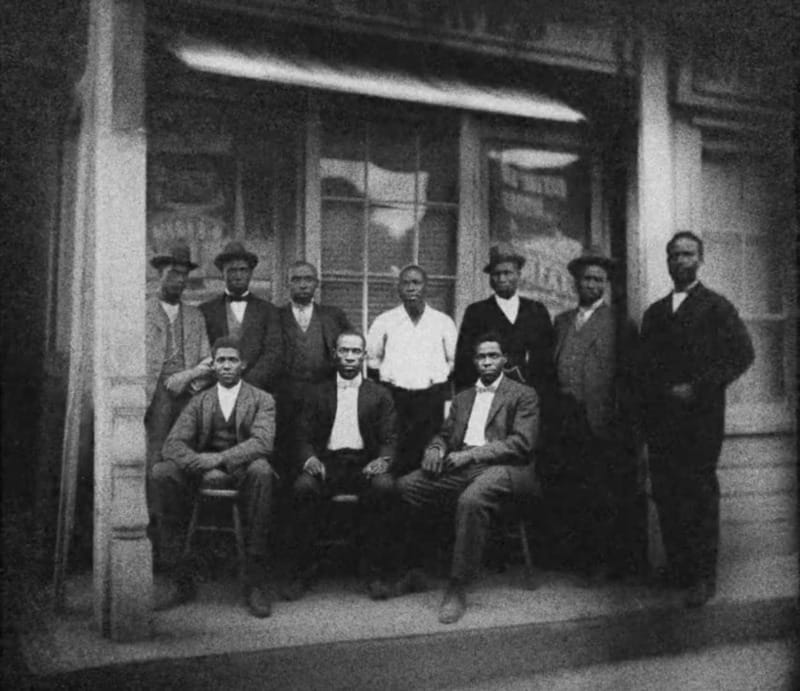 Black and white photo of a group of men in front of a store