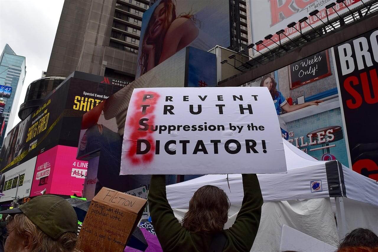 Thought police. People protested him because donald trump is a fascist. Protester holding a sign spelling out ptsd with d standing for dictator.