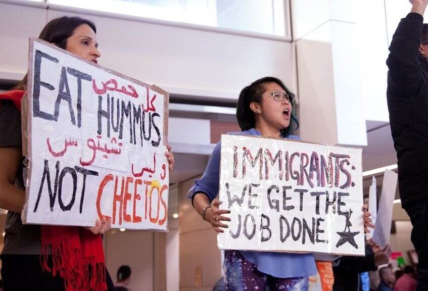 Immigrants protest with a sign that says IMMIGRANTS GET THE JOB DONE