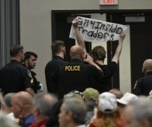 Woman with insider training protest banner at the marjorie taylor greene town hall