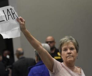 A woman holds up a piece of paper with liar written on it