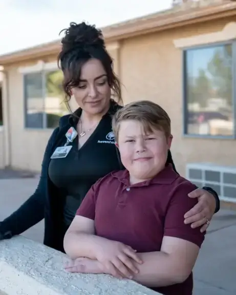 Border security doesn't replace access to medical treatment, mother and son stand side by side with her arm around his shoulder. He smiles at the camera as she looks down at him.