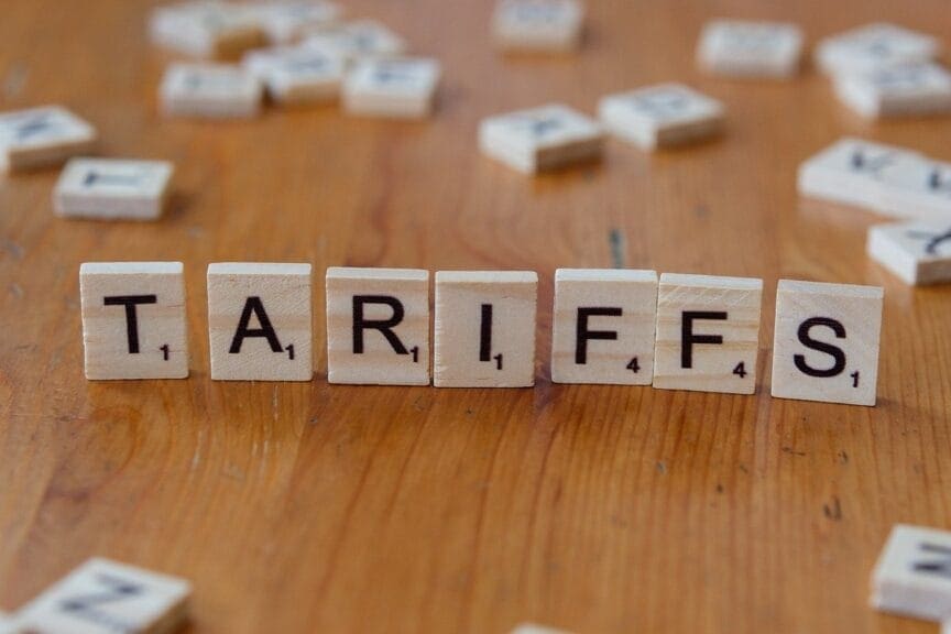 Scrabble tiles standing upright on a wooden table to spell TARIFFS