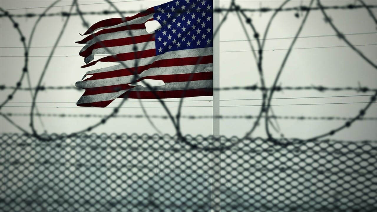 Torn american flag viewed through a fence with razor wire