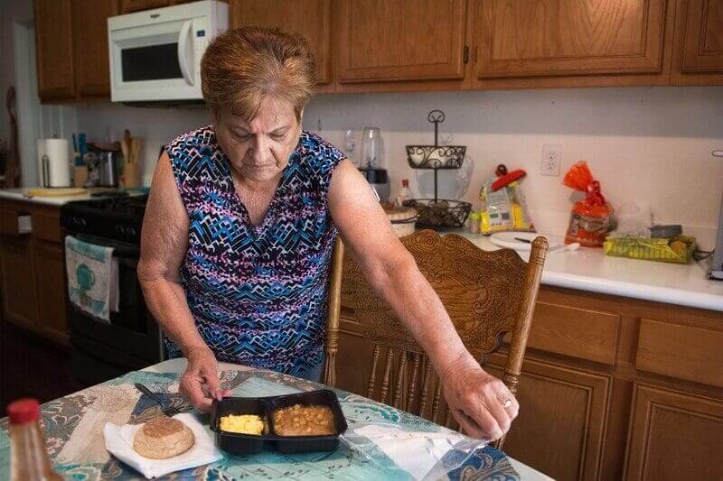Social services elderly woman opening a microwave meal that was covered by medicaid in 2022