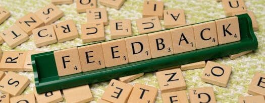 Wooden letter tiles spelling 'feedback' on a green rack, representing communication and evaluation.