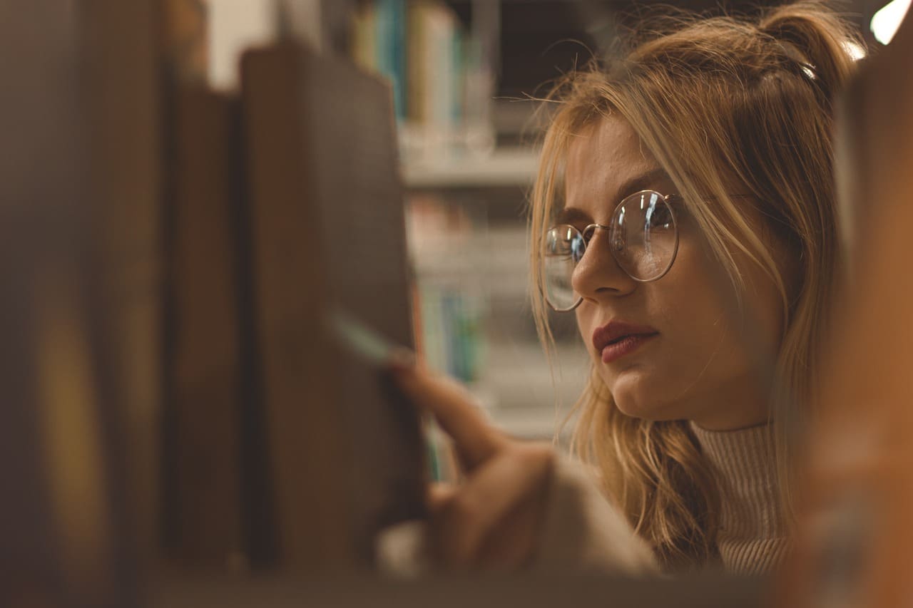 Banned dei books returned to the naval academy library. A girl with glasses looks at books on a library shelf.