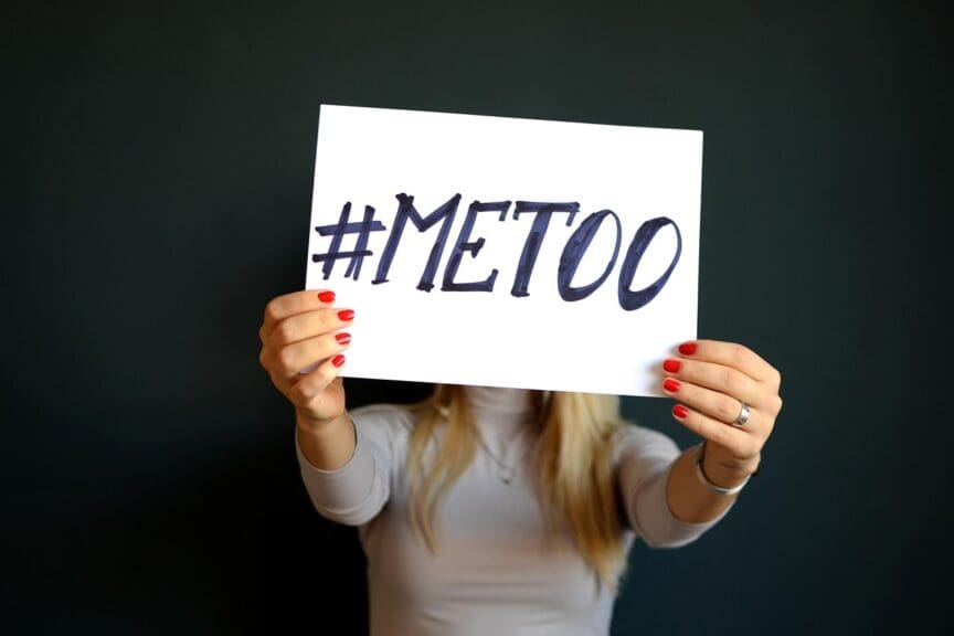 Woman holding a piece of paper with #METOO written on it.