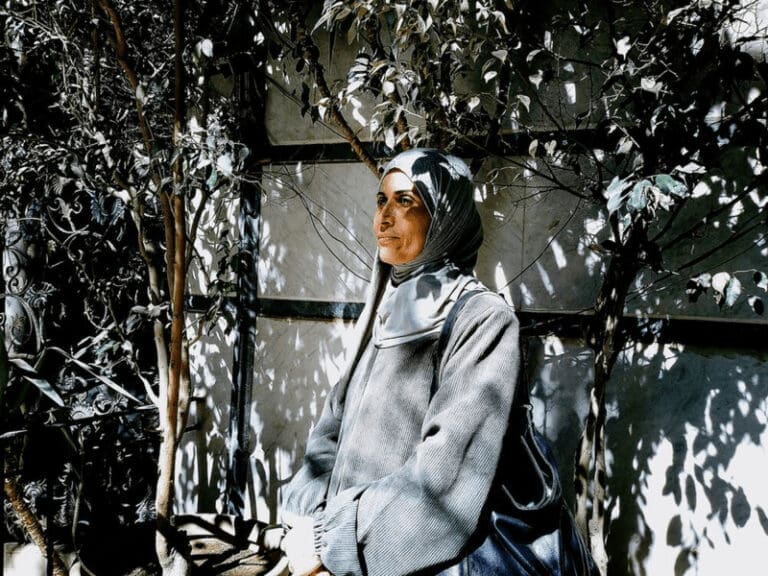 Gazan refugee woman in a hijab standing in the shade of a tree.