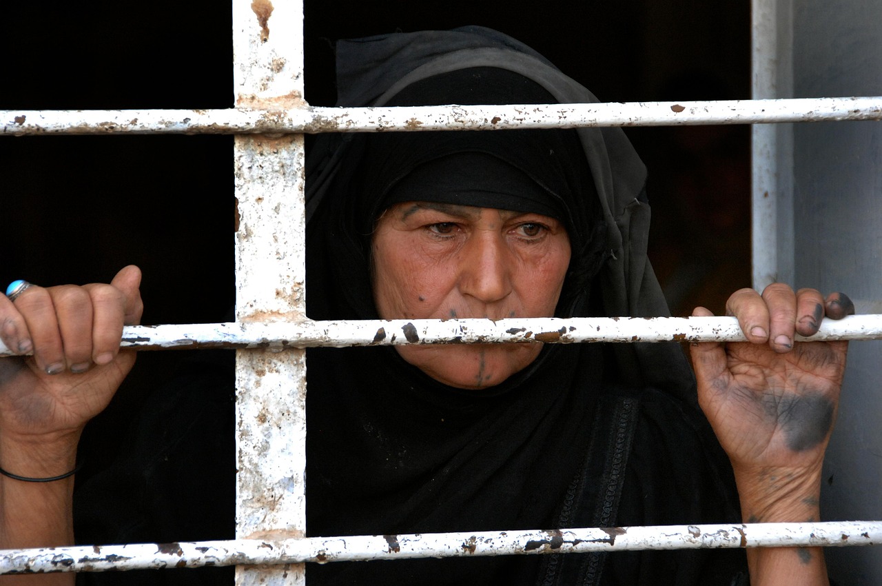 Woman in iraq looking out a bar-covered window
