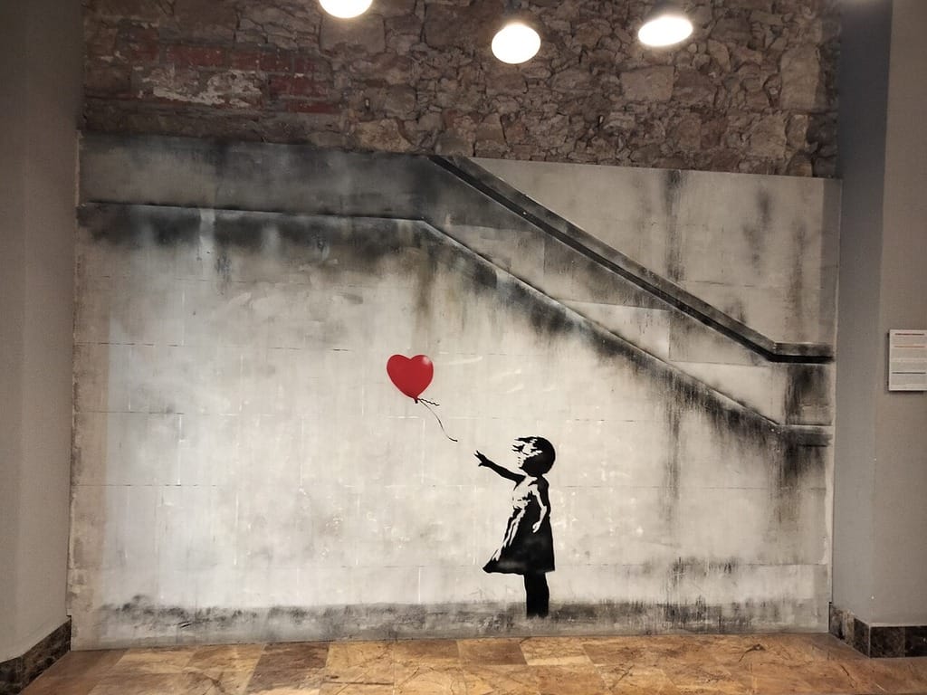 A graffiti art design by Banksy of the little girl holding a red heart balloon.