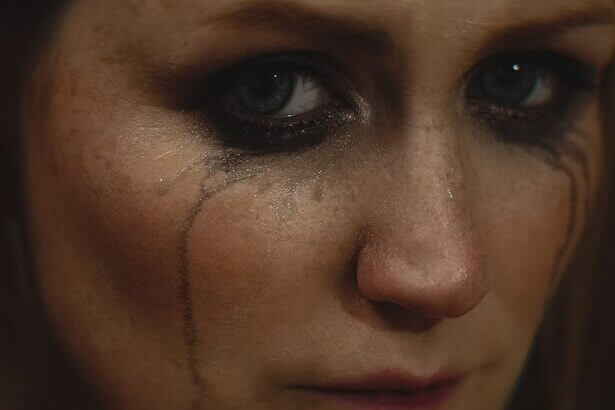 Close-up of a woman with smeared makeup and tears on her face showing deep emotion.