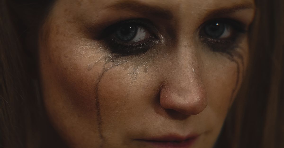 Close-up of a woman with smeared makeup and tears on her face showing deep emotion.