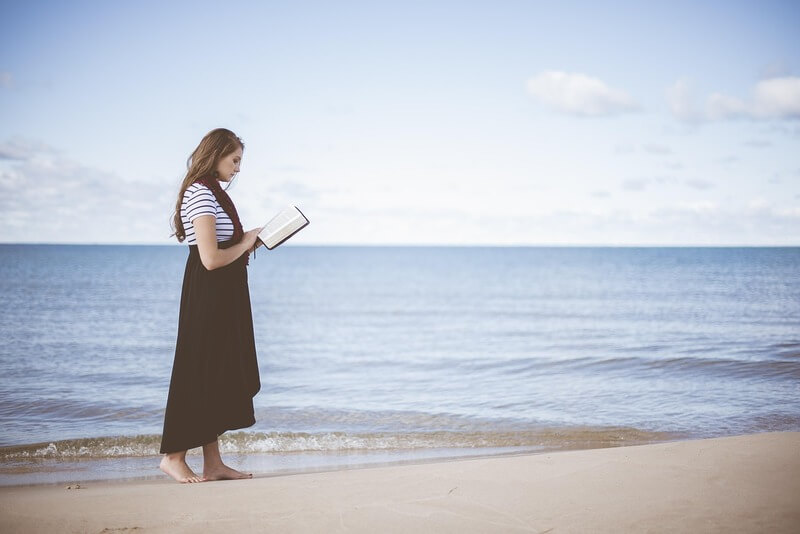 Woman walking on the beach reading a Bible